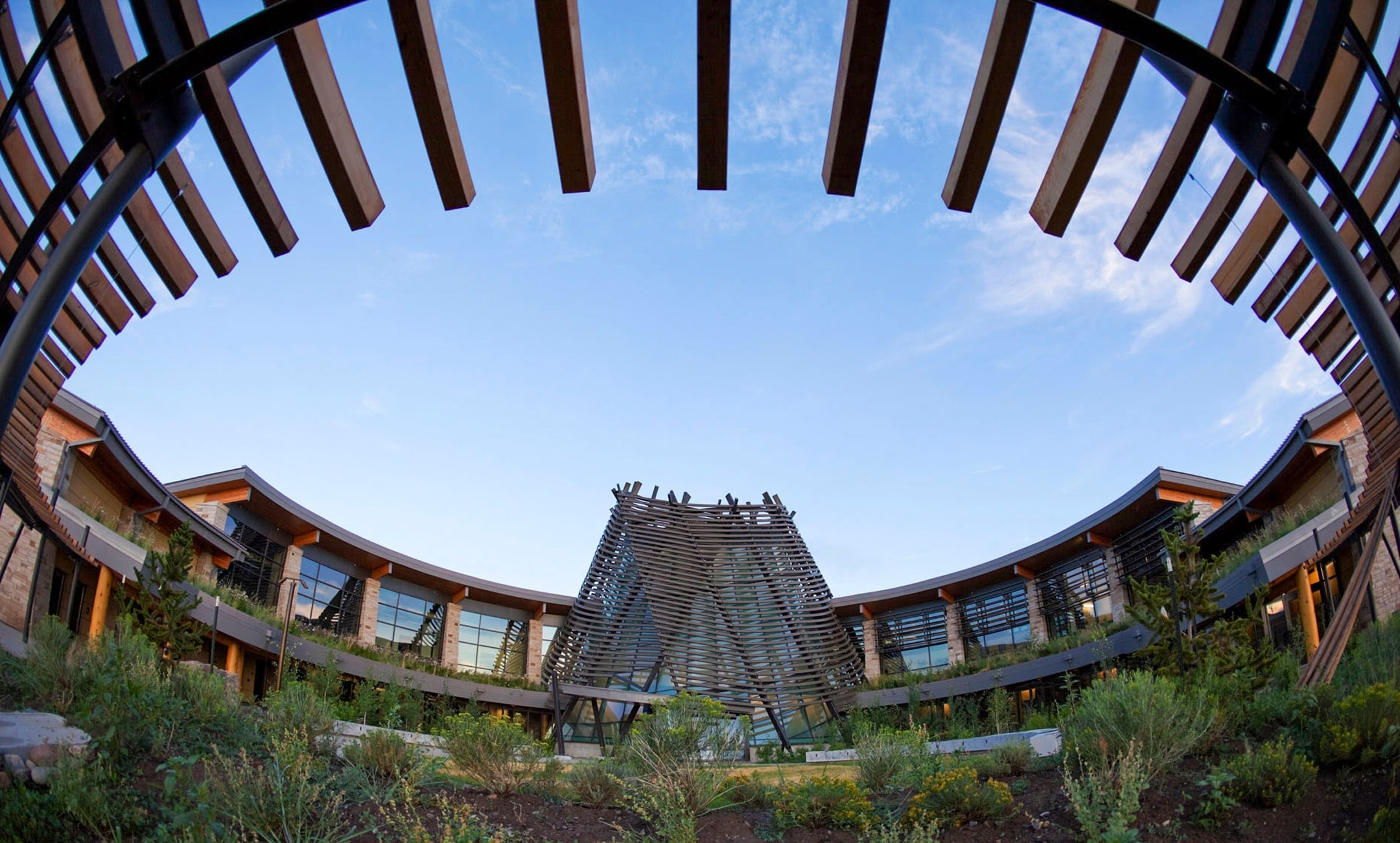 Southern Ute Cultural Center seen through a ring of timber beams, with its slatted conical tower at the center